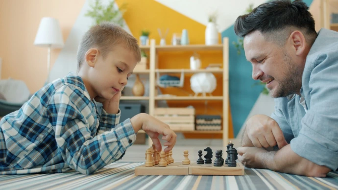 Father and son playing chess on the floor.